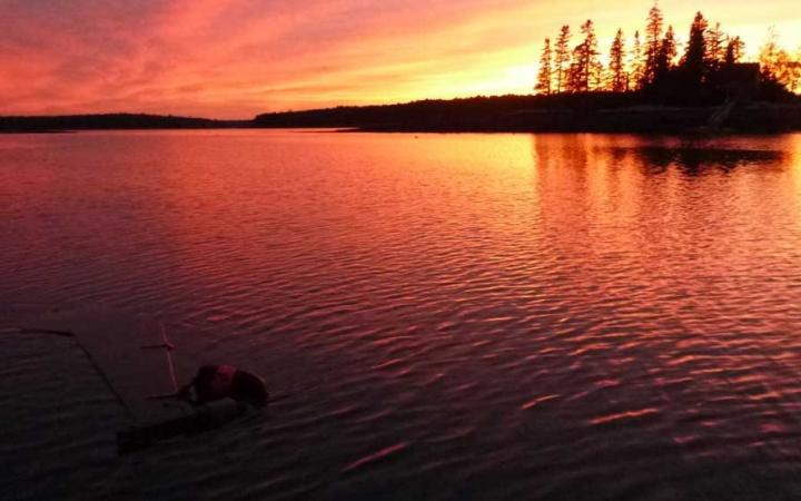 A red, orange and yellow sky is reflected off a calm body of water.